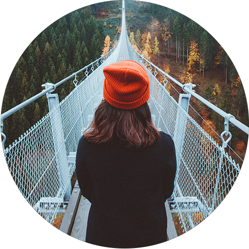 a girl in red beanie hat looking at a long narrow bridge through an evergreen forest