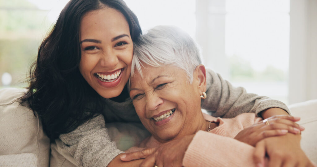 Hug, portrait and smile of old woman with daughter on sofa in living room of home for bonding or visit. Face, family or love with happy woman and senior mother embracing in apartment together